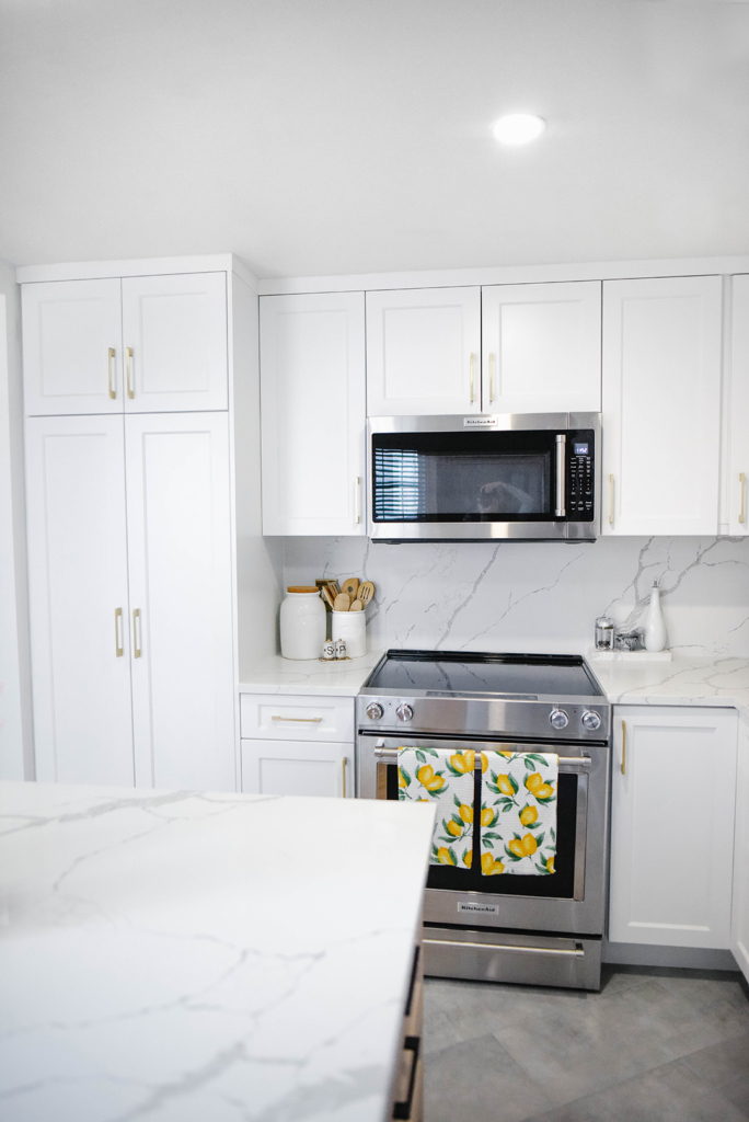 White kitchen wood island with black hardware, marble counter tops, stainless steel appliances