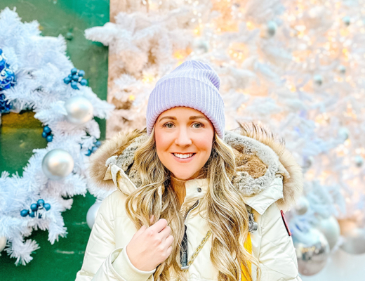 Halifax Influencer Kayla Short poses in front of a green door with a holiday wreath wearing a lilac toque and cream parka